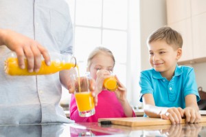 Midsection of father serving orange juice for children in kitchen