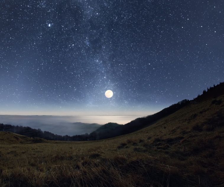 Starry night sky with rising full moon over the misty mountains