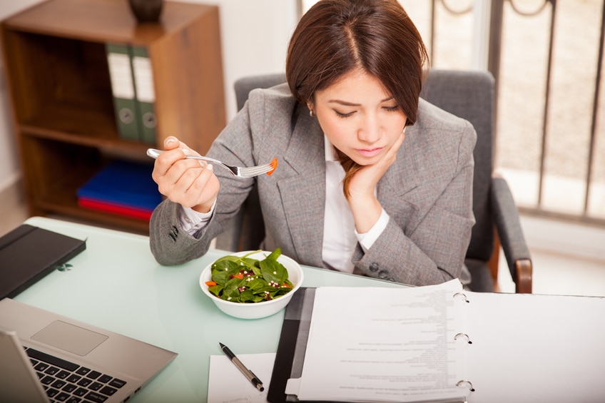 Busy young business woman eating a healthy lunch while working in her office
