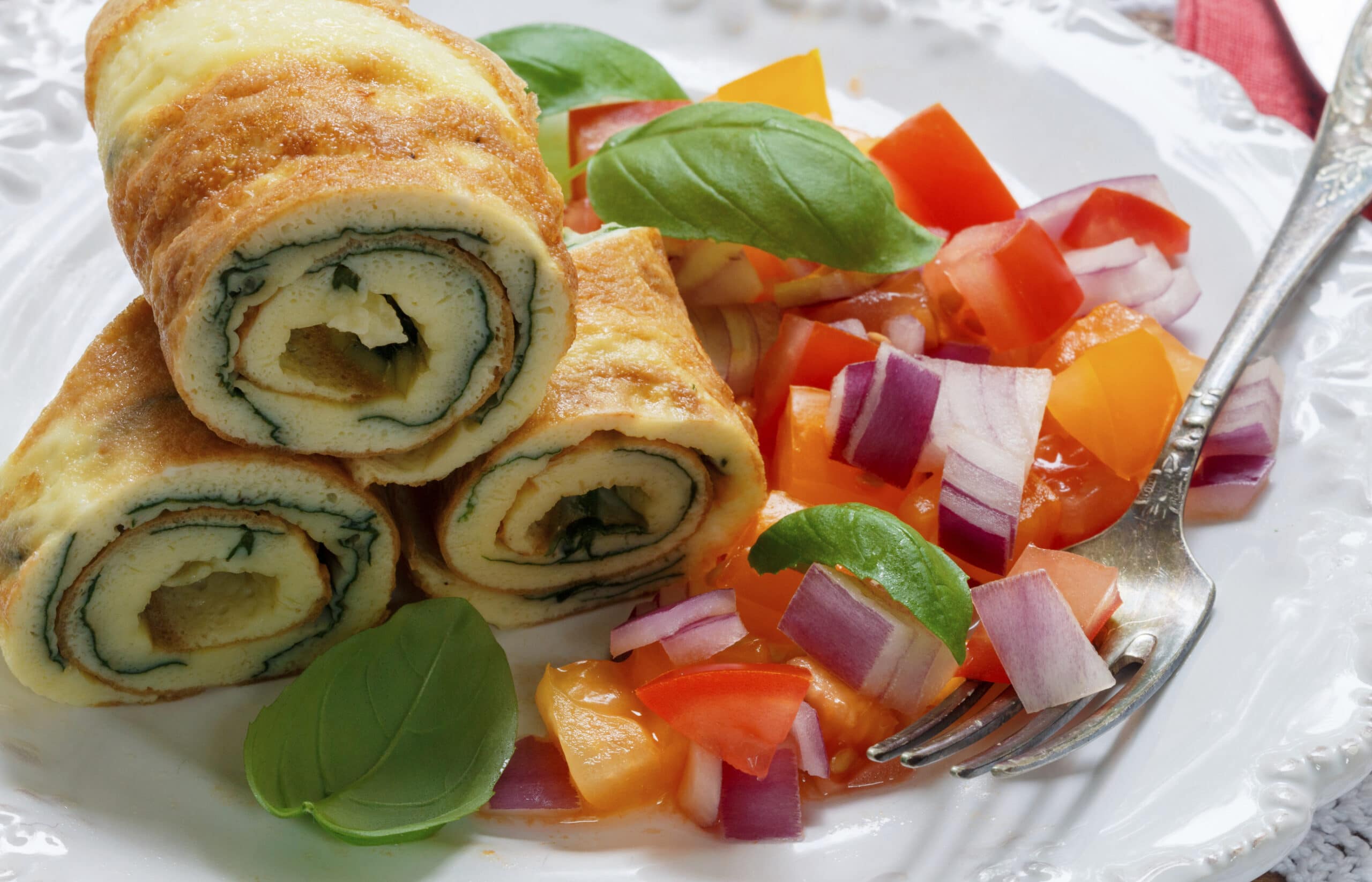 Traditional Breakfast. Omelette with spinach and a fresh tomato salad, red onion and Basil. Roll scrambled eggs. Selective focus