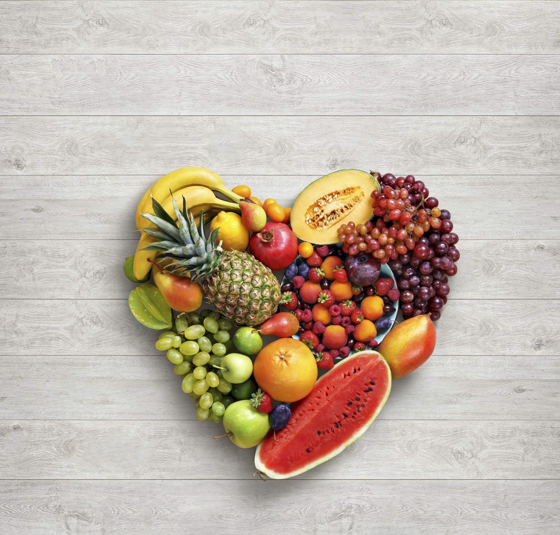 Heart symbol. Fruits diet concept. Food photography of heart made from different fruits on white wooden table. High resolution product.