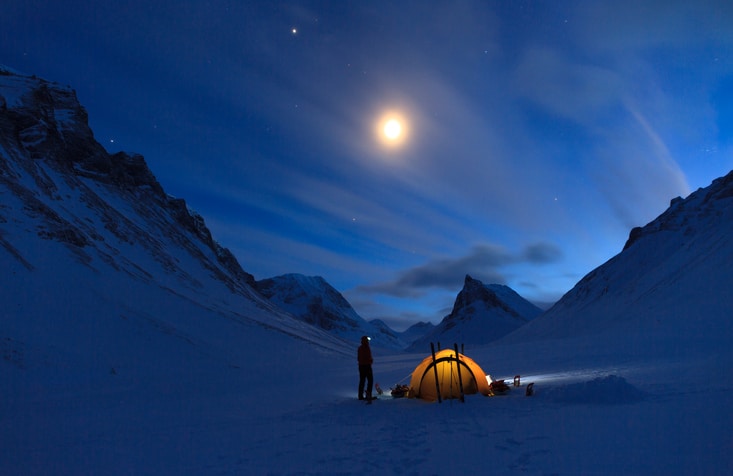 Woman looking at the night sky while camping in the snow covered mountains in Swedish Lapland (Nallo).