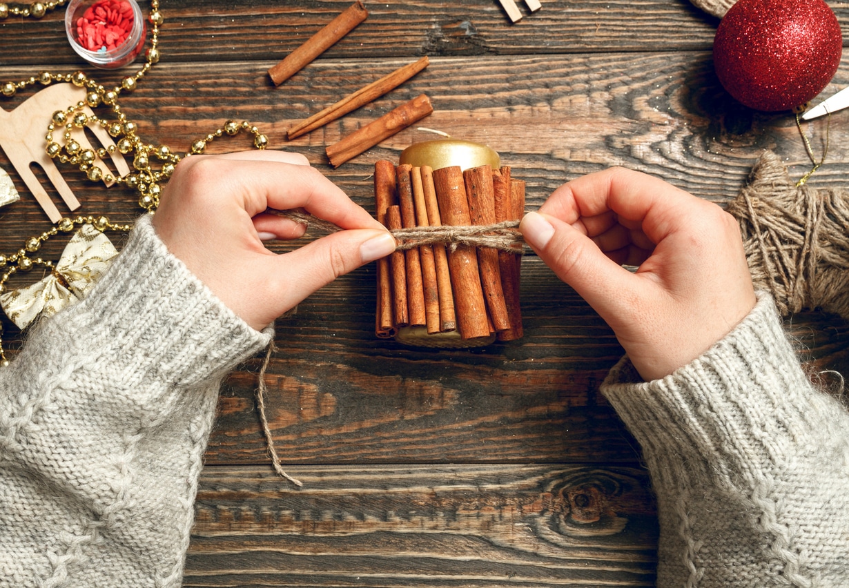 Girl in a bright sweater decorate a candle with using cinnamon